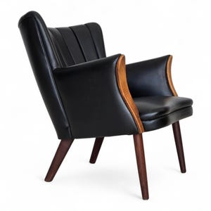 Puede incluir: Sillón de cuero negro con respaldo alto y acanalado y reposabrazos curvos de madera. La silla tiene patas de madera marrón oscuro y un diseño elegante y moderno. Es un mueble elegante.