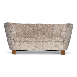 May include: A beige and gold floral patterned sofa. The sofa has a curved back and armrests, and is supported by four wooden legs. The fabric has a textured appearance. The sofa's design is reminiscent of mid-century modern furniture. The sofa measures approximately 180 cm in length.