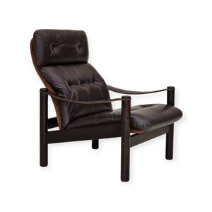 May include: A brown leather armchair with a tufted back and seat. The chair has a dark wood frame and arms with a leather strap detail.