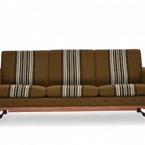 Op de afbeelding: Een bank in mid-century stijl met bruine stof en gestreepte kussens en rugleuning. Het heeft houten armleuningen en poten. De kussens en rugleuning hebben verticale crème en bruine strepen. Ongeveer 200 cm lang.