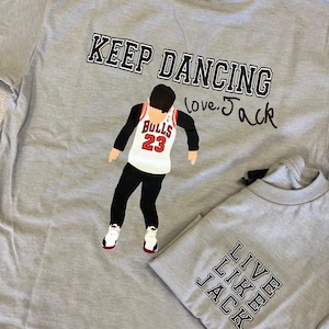 May include: Two gray t-shirts. One features a graphic of a basketball player in a Bulls jersey with the text "KEEP DANCING love Jack". The other shirt says "LIVE LIKE JACK".