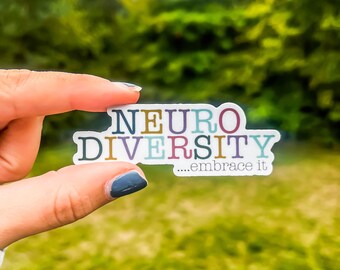 May include: A white sticker with the words "NEURO DIVERSITY...embrace it" in colorful letters. The sticker is being held by a finger against a blurred background of green trees.