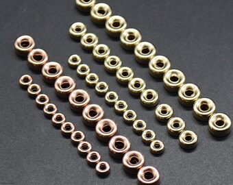 Può includere: Assortimento di perline in metallo dorato e oro rosa con un foro al centro. Le perline sono disposte in file dal più grande al più piccolo.