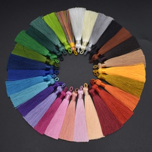 Puede incluir: Una colección de 20 borlas de seda de colores dispuestas en círculo sobre un fondo negro. Las borlas están hechas de un material suave y sedoso y están disponibles en una variedad de colores, incluyendo rojo, naranja, amarillo, verde, azul, morado y rosa.