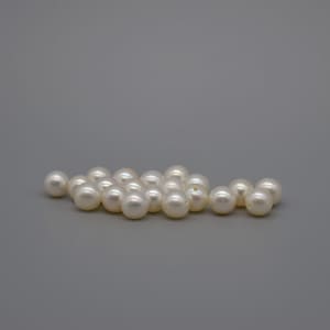 May include: A group of white pearls scattered on a grey background. The pearls are round and smooth, with a slight iridescent sheen.