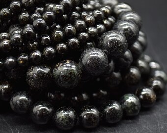 May include: A close-up of a pile of black gemstone beads with a speckled, glittery texture. The beads are round and smooth, and they are arranged in a random pattern.