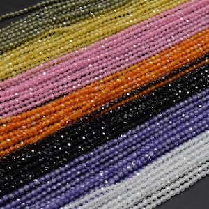 May include: Assortment of faceted gemstone beads in various colours, including green, yellow, pink, orange, black, purple, and white. The beads are strung on a thread and are arranged in rows.