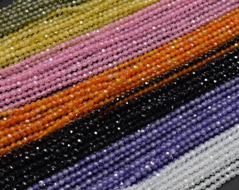 May include: Assortment of faceted gemstone beads in various colors, including green, yellow, pink, orange, black, purple, and white. The beads are strung on a thread and are arranged in rows.