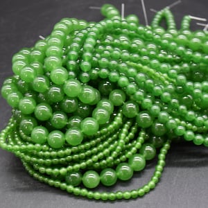 May include: A pile of green jade beads of various sizes. The beads are smooth and polished, and they are arranged in a random pattern.
