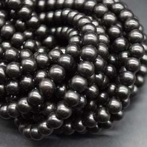 May include: Close-up of a strand of dark gray, glossy beads. The beads are spherical and appear to be strung together, forming a necklace or bracelet. The beads have a smooth, reflective surface, and the overall effect is one of elegance and sophistication.