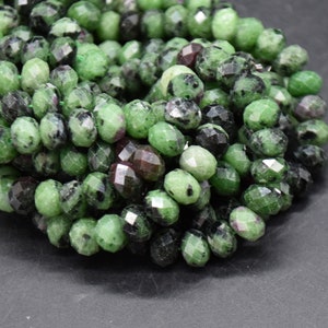 May include: A strand of green, black and red faceted gemstone beads. The beads are oval shaped and have a smooth, polished finish.