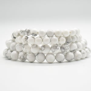 May include: A stack of white howlite bead bracelets. The beads are round and have a marbled pattern.