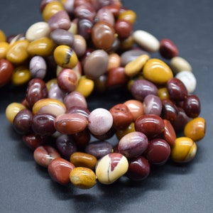 Puede incluir: Un collar o pulsera compuesto por cuentas ovaladas pulidas. Las cuentas son de varios colores, incluyendo rojo, marrón, amarillo y crema. Las cuentas están ensartadas y tienen un acabado liso y brillante.