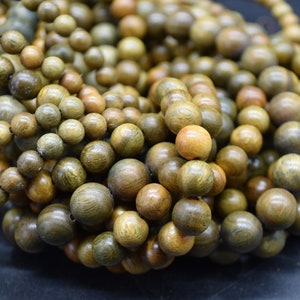 May include: A close-up of a pile of round, wooden beads. The beads are a mix of brown and green colours, with some having a darker, almost black, hue. The beads are smooth and polished, and they have a natural, organic look.