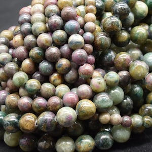 May include: A close-up of a pile of round, green, brown, and pink gemstone beads. The beads are smooth and have a speckled appearance.