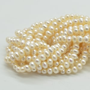 May include: A strand of white freshwater pearls, with a smooth, oval shape. The pearls are arranged in a loose pile, showcasing their natural beauty.