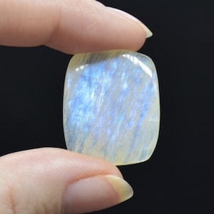 May include: A pale blue and white moonstone cabochon with a smooth, polished surface. The stone is iridescent and has a subtle shimmer.