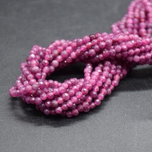 May include: A strand of pink faceted gemstone beads. The beads are small and round, and they are strung together on a clear thread.