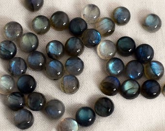 May include: A collection of round, iridescent labradorite cabochons in shades of blue, gray, and black. The stones are smooth and polished, with a subtle shimmer.