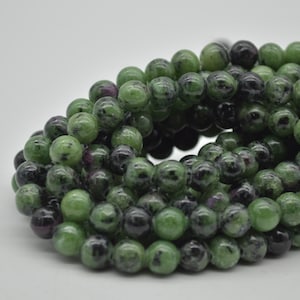 May include: A strand of green, black, and pink gemstone beads. The beads are round and have a speckled appearance.