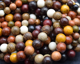 May include: A close-up of a collection of wooden beads in various colors and textures. The beads range in shades from light beige and white to dark brown and black, with some featuring wood grain patterns. The beads are spherical and appear to be of varying sizes.
