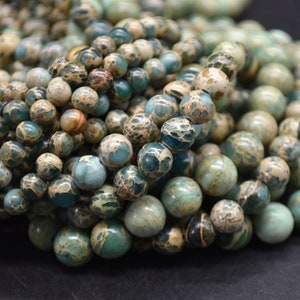 May include: Close-up of a collection of round beads in shades of green, teal, and cream. The beads have a speckled pattern, with variations in colour and texture. These beads are suitable for jewellery making.