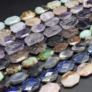 Könnte beinhalten: Eine Auswahl an Edelsteinperlen in verschiedenen Farben und Mustern, darunter Amethyst, Achat und Lapislazuli. Die Perlen sind facettiert und haben eine polierte Oberfläche. Sie sind in Reihen angeordnet, wobei die größten Perlen oben und die kleinsten unten liegen.