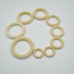 May include: A set of ten wooden rings in various sizes, arranged in a circle on a white background. The rings are all natural wood colour and have a smooth, polished finish.