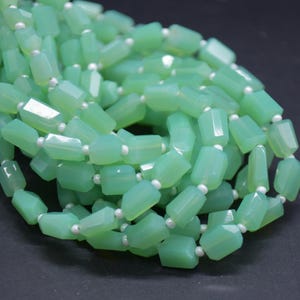 May include: A strand of faceted, light mint green beads arranged in a loose, coiled pile. Each translucent, rectangular bead is separated by a small, round, opaque white spacer bead, creating a repeating pattern throughout the entire length.