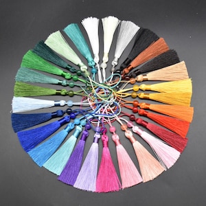 May include: A collection of 24 colourful silk tassels with beads. Each tassel is approximately 5 cm long and features a variety of colours, including red, blue, green, yellow, and purple.