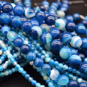 May include: A close-up of a pile of blue and white agate beads. The beads are round and have a smooth, polished finish. They are ideal for making jewellery or other crafts.