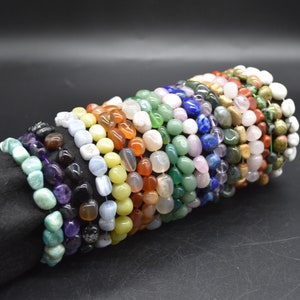 May include: A stack of colorful gemstone bracelets, each featuring a different type of stone. The bracelets are made with smooth, rounded beads and are arranged in a rainbow pattern.