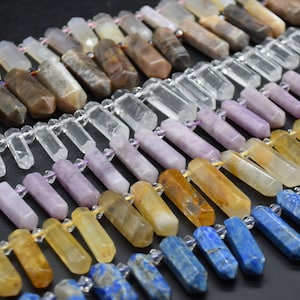 May include: A collection of gemstone beads in various colors, including clear, purple, yellow, and blue. The beads are faceted and have a pointed shape. They are arranged in rows, with the colors transitioning from light to dark.