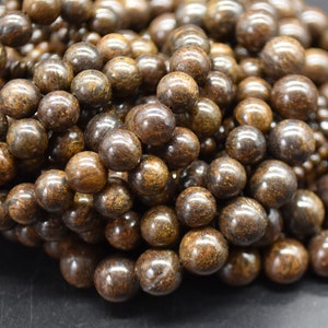 Puede incluir: Primer plano de un montón de cuentas de madera marrón y negro. Las cuentas son redondas y tienen un acabado liso y pulido.