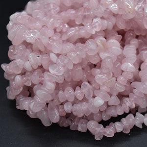 以下が含まれることがあります： ピンクのローズクォーツチップビーズのストランド。ビーズは不規則な形をしていて、滑らかで磨かれた仕上げになっています。