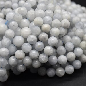 May include: A close-up of a pile of light blue round gemstone beads. The beads are smooth and polished, with a slightly translucent appearance.