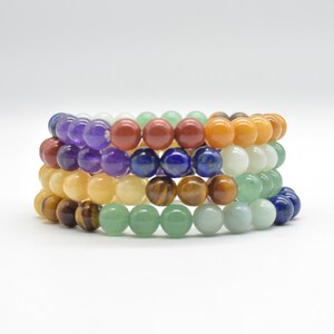 Puede incluir: Una pila de siete pulseras de cuentas de colores, cada una con un color y tipo de piedra diferente. Las pulseras están hechas de amatista, jaspe rojo, cornalina, aventurina, lapislázuli, ojo de tigre y aventurina verde.