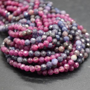 May include: A strand of faceted gemstone beads in shades of pink, blue, and purple. The beads are round and have a slightly irregular shape.