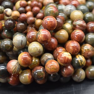 May include: A close-up of a strand of round, multi-colored gemstone beads. The beads are a mix of brown, red, and green with swirling patterns.