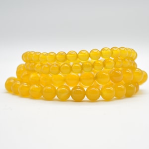 May include: Four strands of yellow beaded bracelets are stacked. The beads are round and glossy. The bracelets are a bright, sunny yellow colour. The beads are approximately 0.6 cm in diameter.