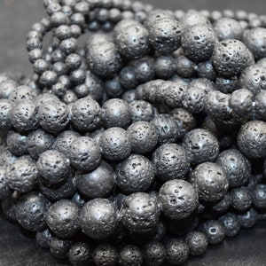 May include: A close-up of a pile of black lava rock beads. The beads are round and have a rough, textured surface.