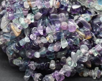 May include: A strand of multi-colored fluorite chip beads. The beads are a mix of purple, blue, and green, and they are all tumbled and polished. The beads are strung on a clear elastic cord.