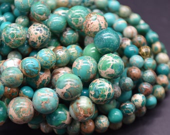 Peut inclure: Gros plan sur un brin de perles de jaspe vertes et brunes. Les perles sont rondes et ont un aspect marbré.