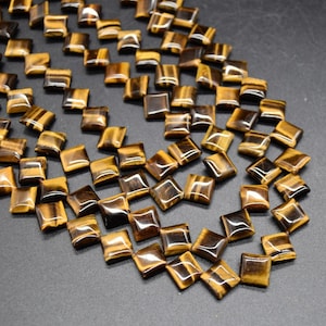 May include: A strand of square-shaped tiger's eye beads. The beads are a mix of golden brown and black colours with a glossy finish.