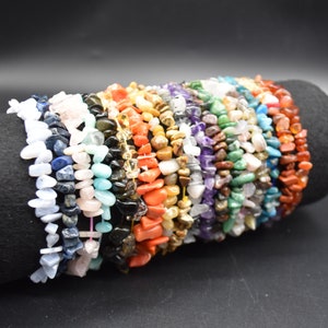 Può includere: Una pila di braccialetti colorati in pietra. I braccialetti sono realizzati con vari tipi di pietre, tra cui ametista, quarzo rosa, turchese e diaspro.