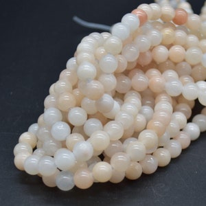 May include: A strand of white and peach-coloured round beads. The beads are made of natural stone and have a smooth, polished finish.