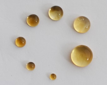 May include: Seven round, translucent, amber-colored glass cabochons of varying sizes on a white background.