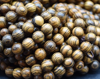 May include: A close-up of a pile of dark brown wooden beads with black and yellow stripes. The beads are round and smooth, and they are arranged in a random pattern.