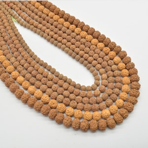 May include: A strand of brown and beige round beads with a textured surface. The beads are strung on a thin cord.