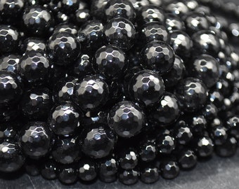 May include: A close-up of a pile of black faceted gemstone beads. The beads are round and have a shiny, polished finish.